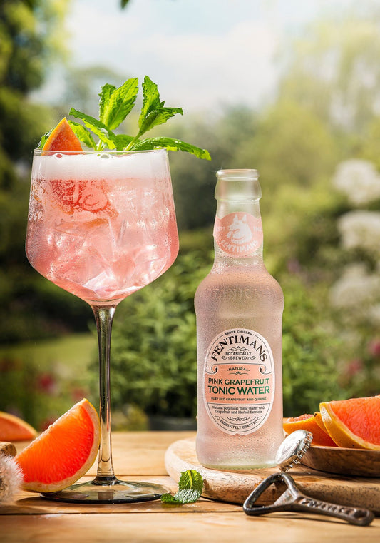 A serve in a balloon glass garnished with grapefruit beside a bottle of Fentimans Pink Grapefruit Tonic Water