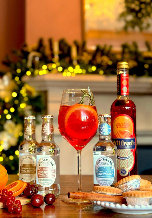 An orange spritz garnished with an orange slice in a festive setting sat beside Fentimans mixers and Wilfreds Aperitif